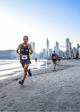 Sidney correndo em uma praia com prédios atrás